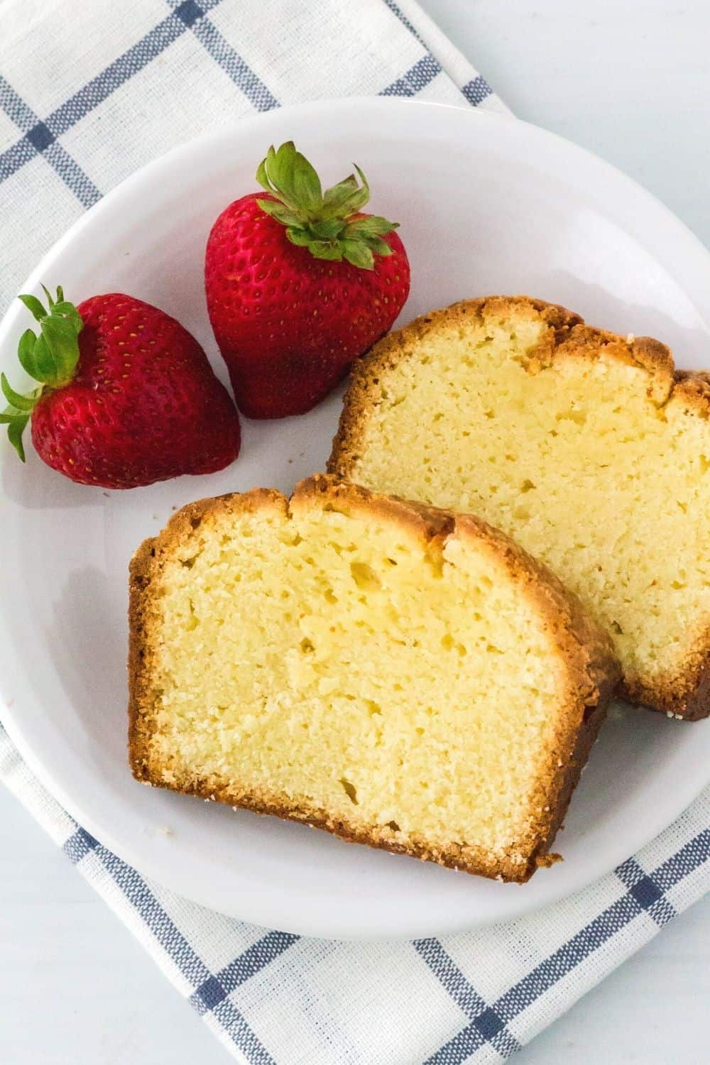 overhead view of two slices of cream cheese loaf cake served on a white plate alongside two fresh strawberries
