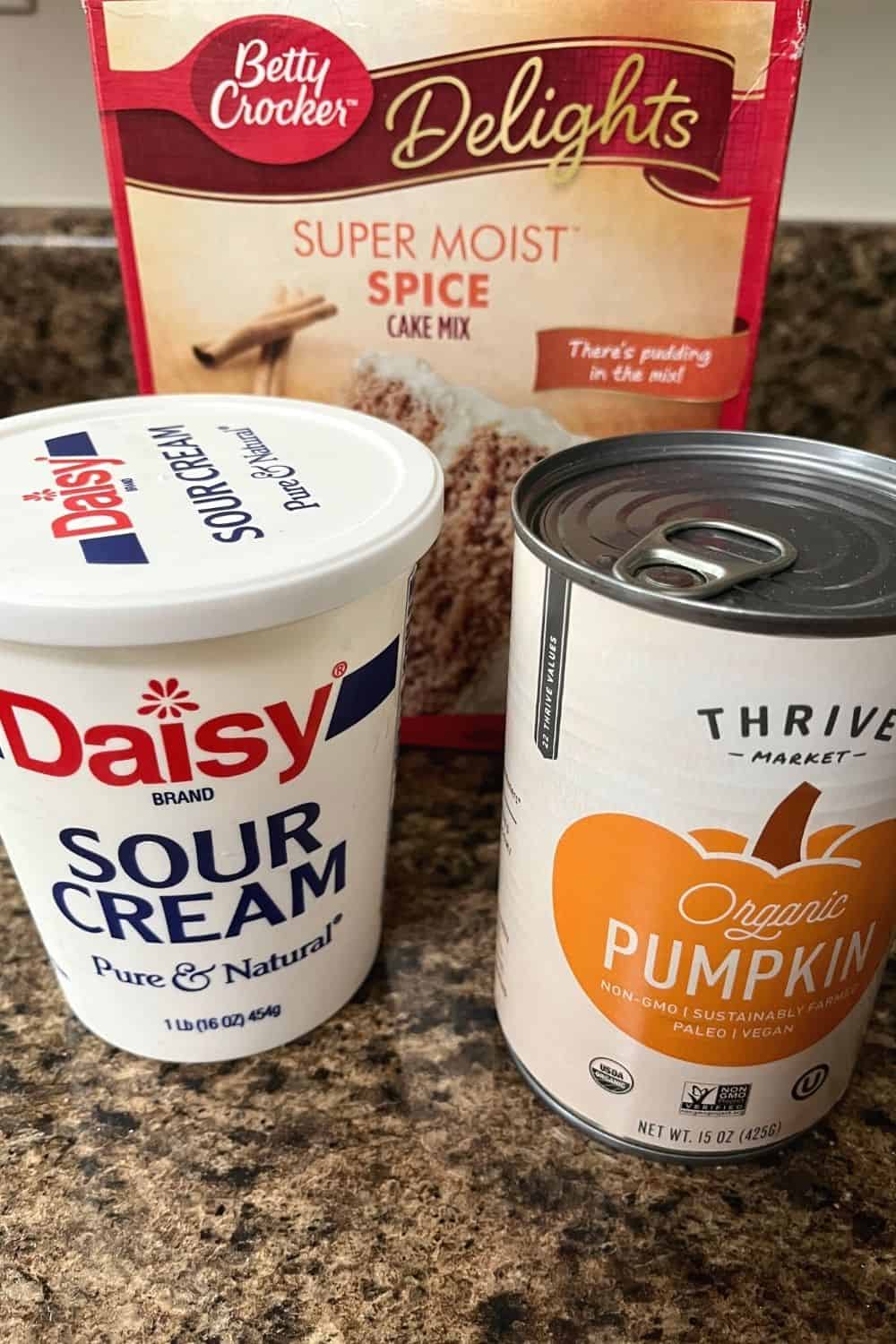 photo showing the ingredients for pumpkin muffins, including a box of spice cake mix, a can of pumpkin puree, and some sour cream
