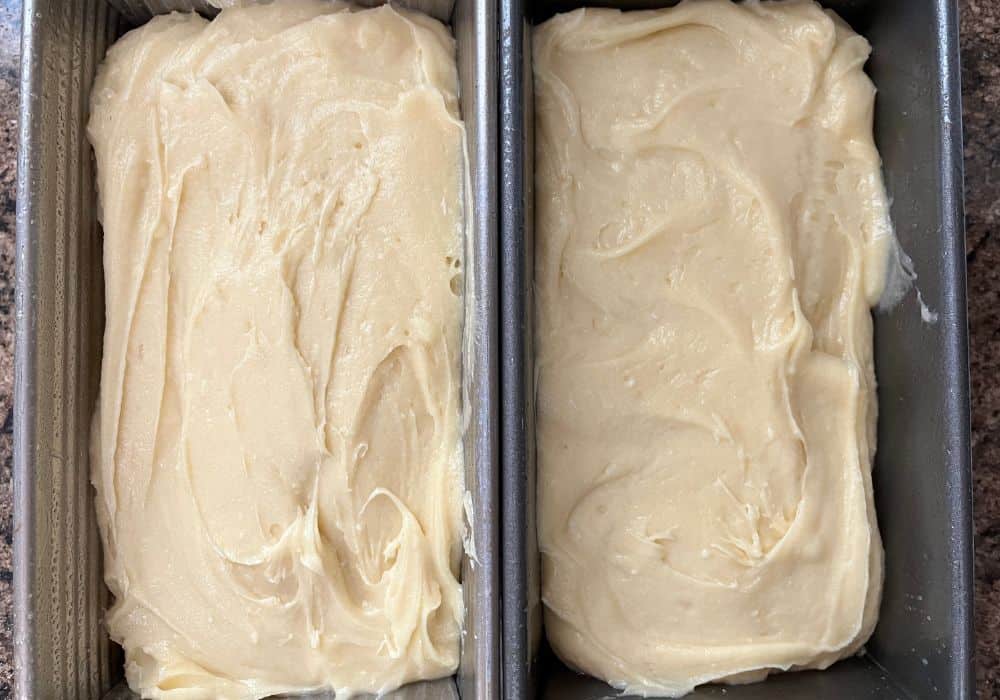 Two greased loaf pans with cream cheese pound cake batter in them, ready to be baked.