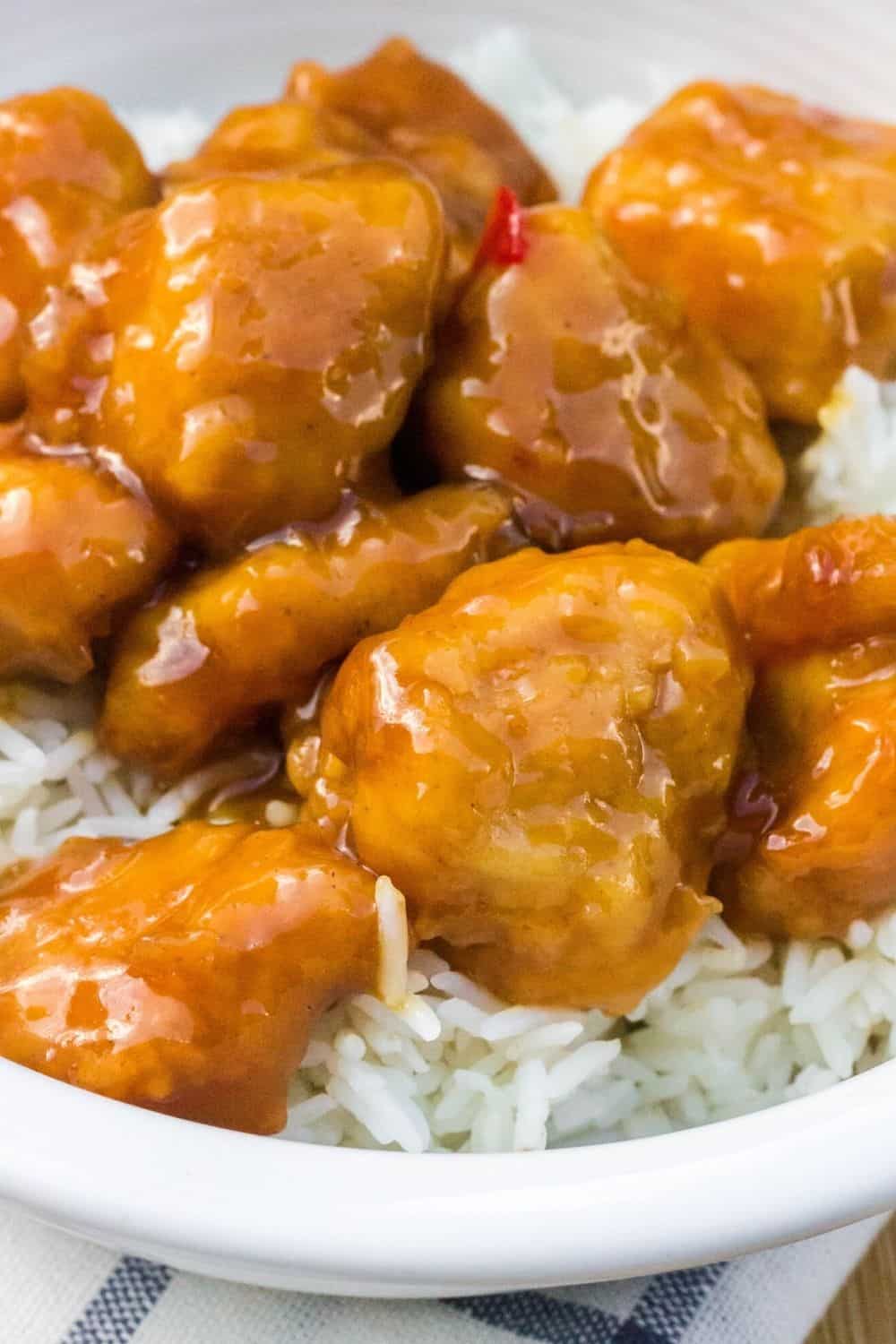 orange chicken cooked in the air fryer, served over white rice in a white bowl