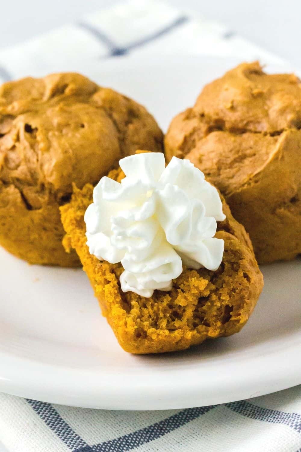 a half of a cake mix pumpkin muffin, topped with whipped cream, on a plate with two other whole muffins