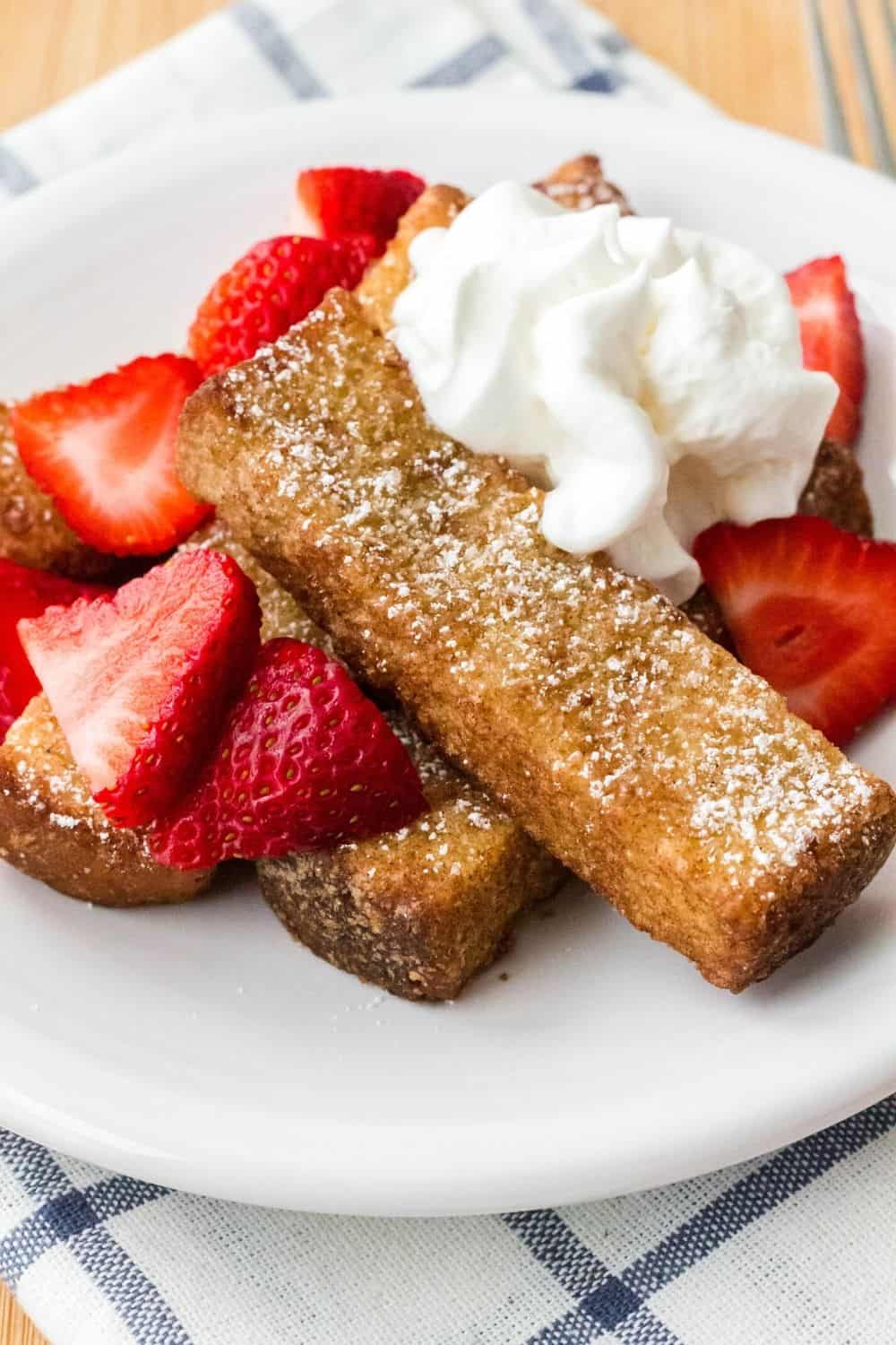 air fryer french toast sticks with fruit and cream served on a white plate
