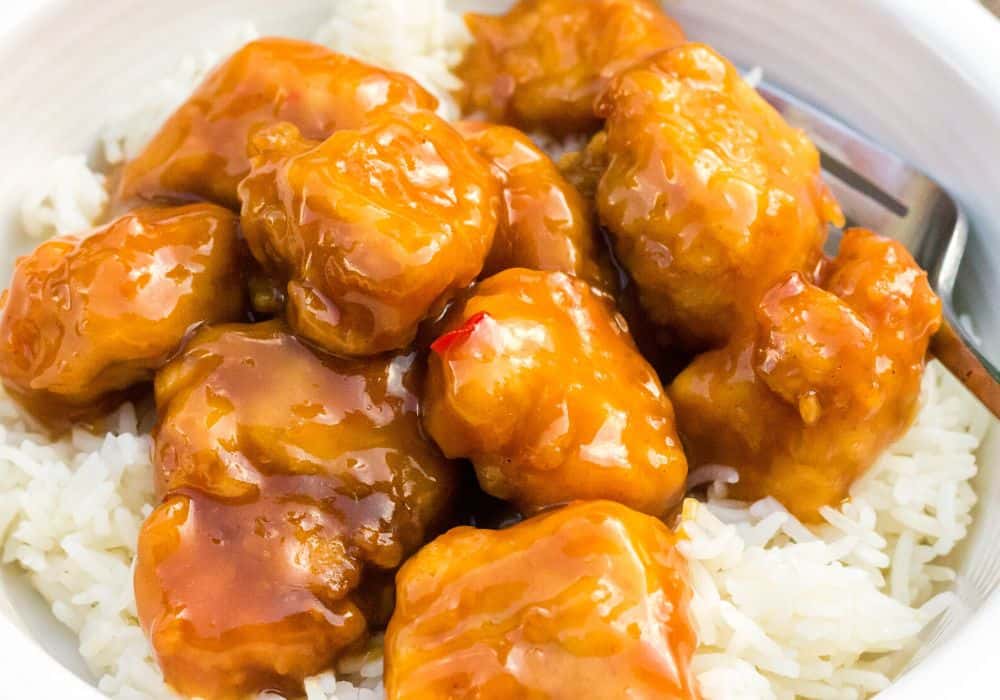 air fryer orange chicken close-up view, served over rice in a white bowl, with a fork in the bowl