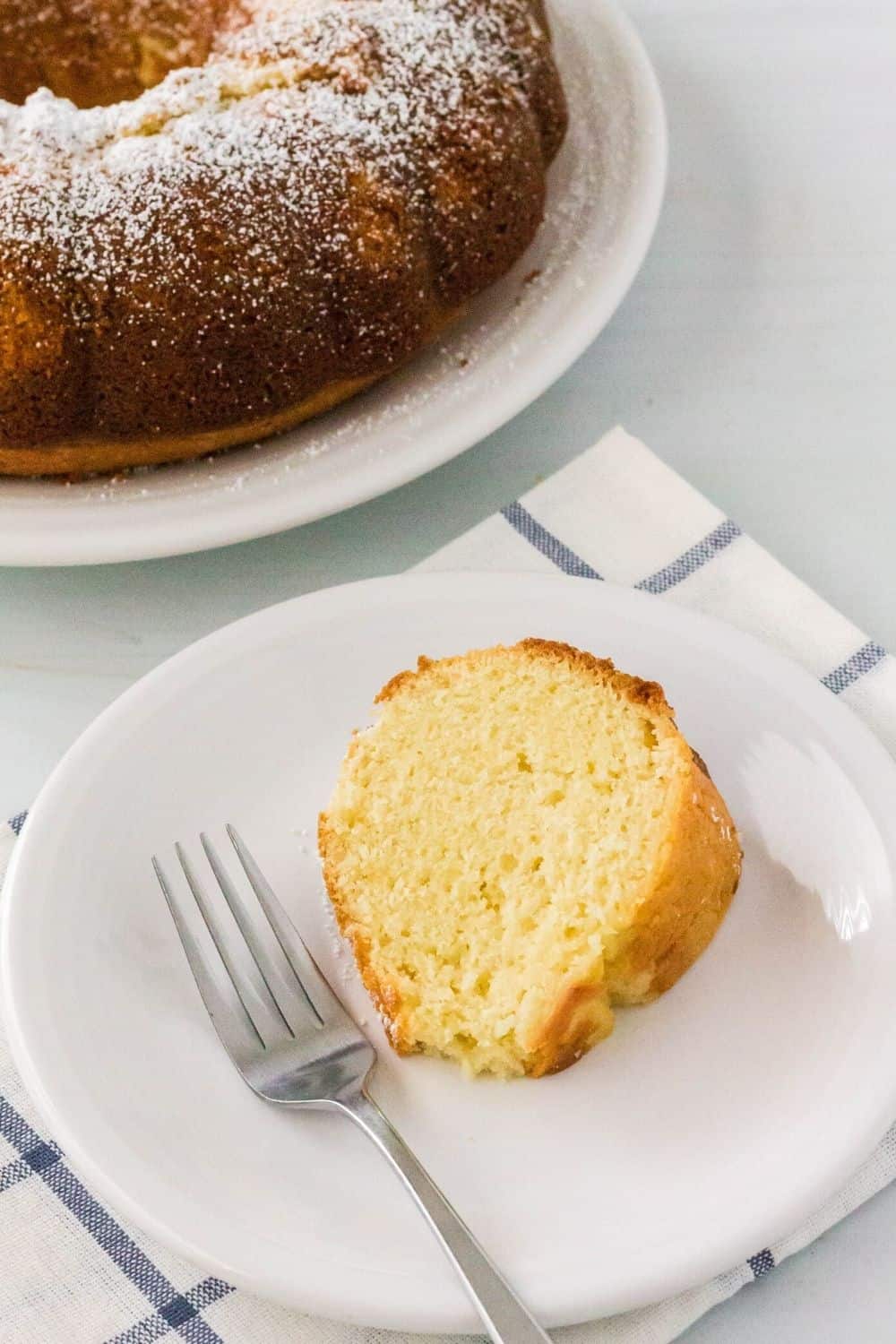 a slice of vanilla mayonnaise cake on a white plate, with the remaining bundt cake in the background