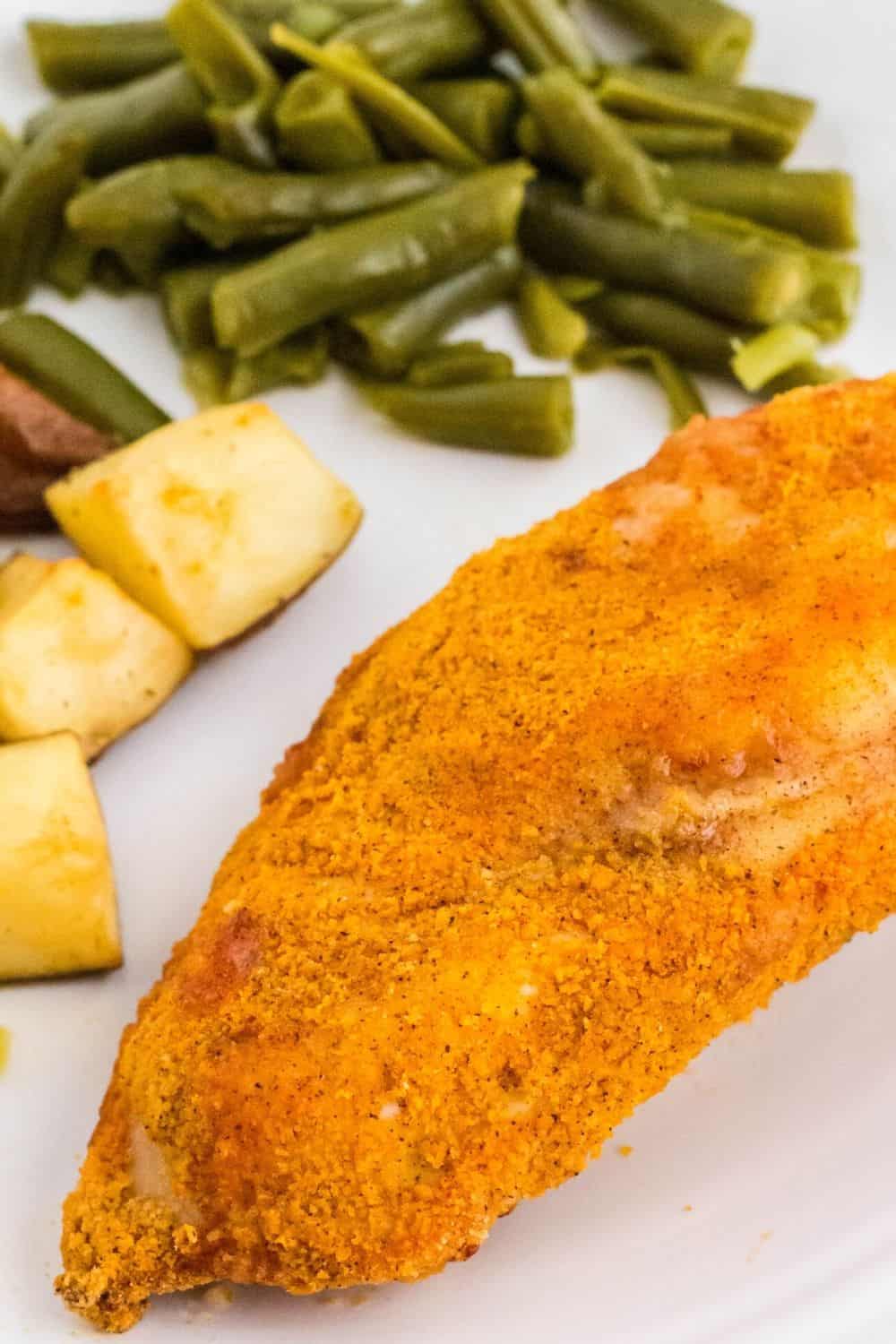 air fryer shake and bake chicken breast on a white plate with side dishes of potatoes and green beans
