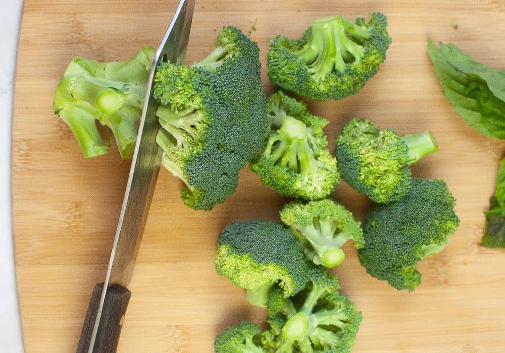 a knife cuts broccoli into florets