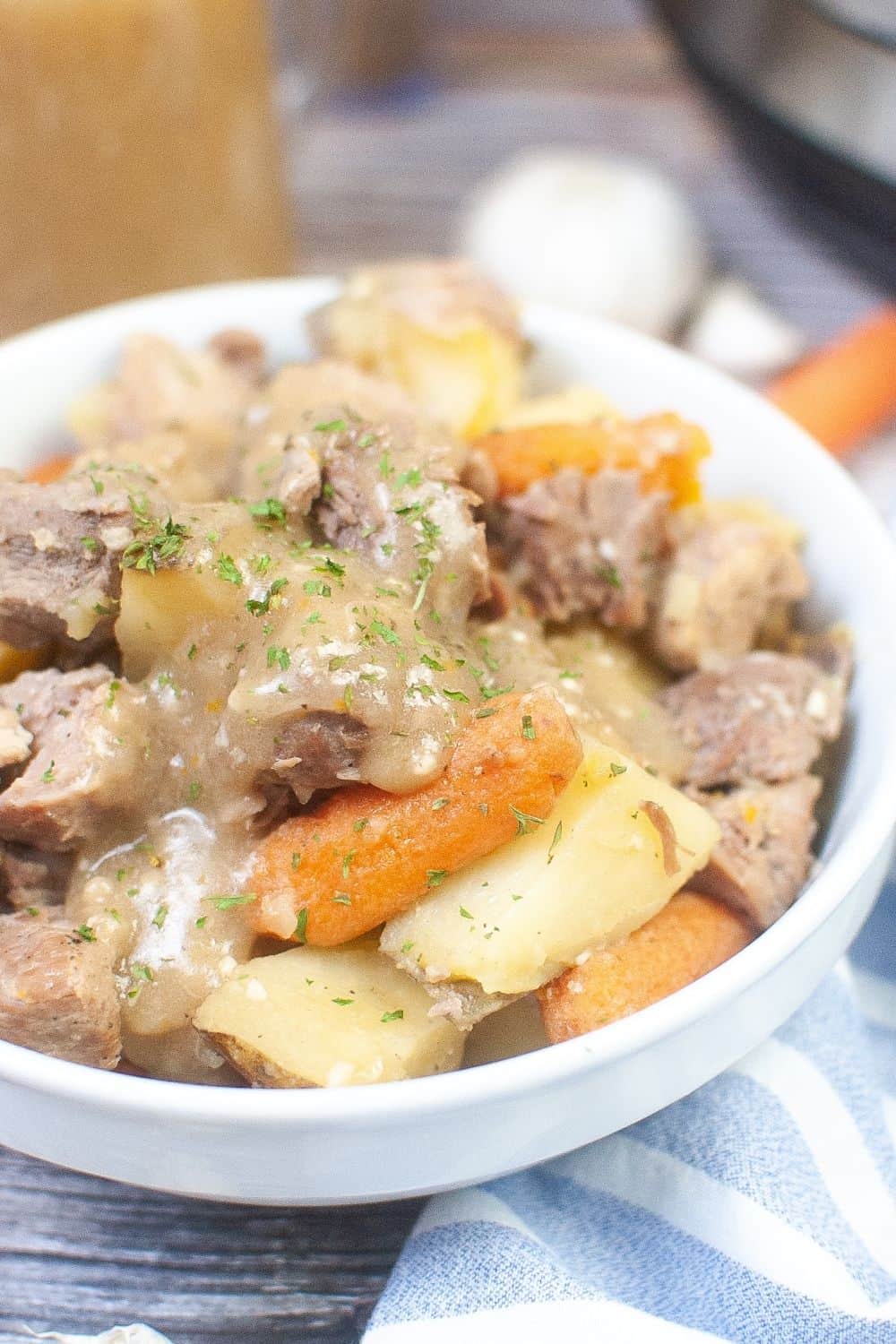 close-up view of Instant Pot pork roast cooked with carrots and potatoes, served with gravy in a white bowl