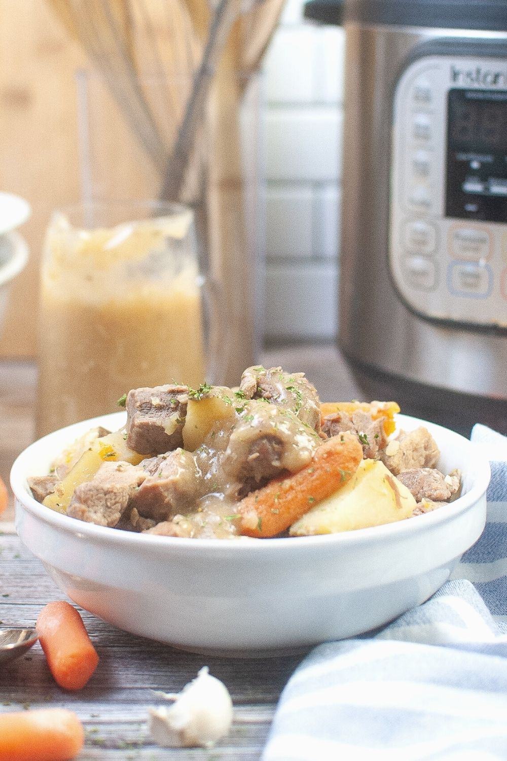 white bowl of pressure cooker pork roast, carrots, and potatoes in front of an instant pot