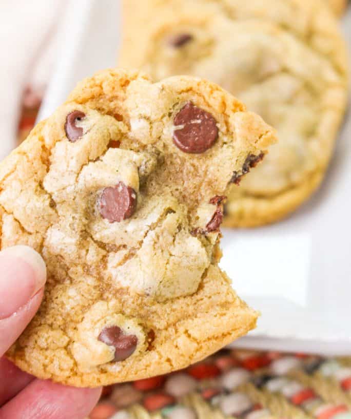 a woman's hand holds a no butter chocolate chip cookie with a bite taken out of it