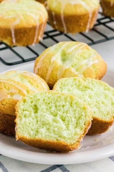 pistachio muffins served on a white plate. One muffin is cut in half to show moist interior.