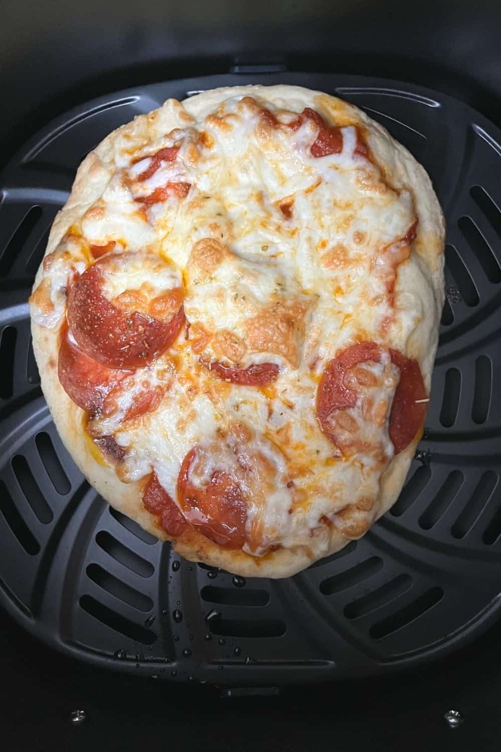 freshly baked naan pizza in the basket of an air fryer, with golden melted cheese