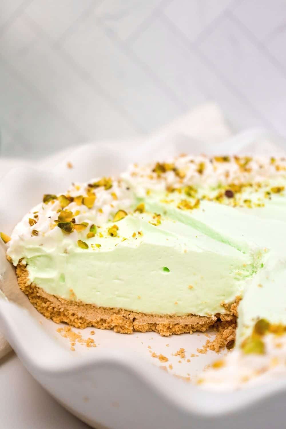 close-up side view of pistachio cream pie in a dish, garnished with whipped cream and chopped pistachios