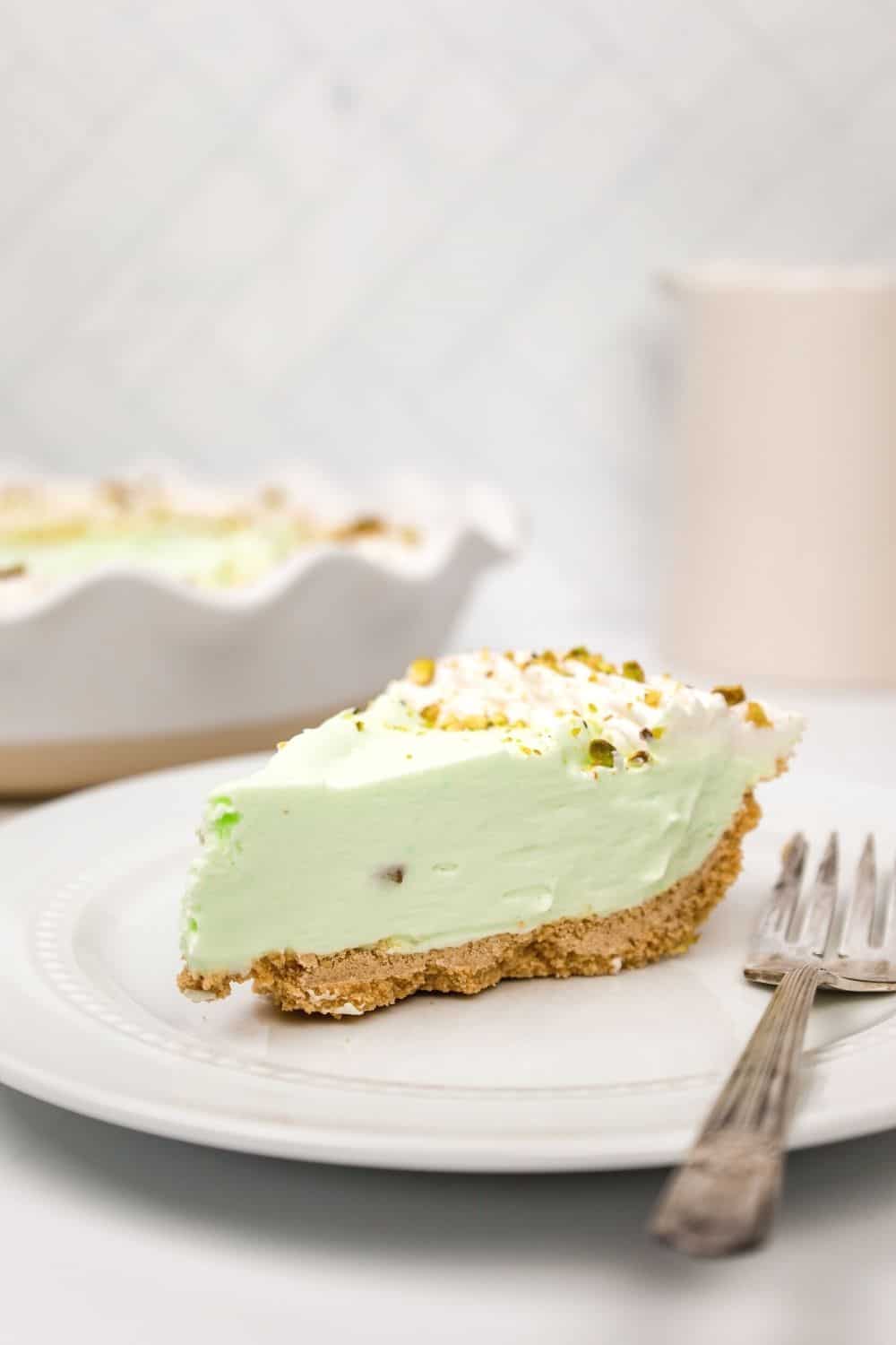 side view of a slice of creamy pistachio pie on a white plate with a fork