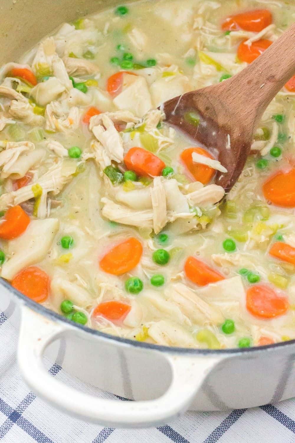 a dutch oven filled with a batch of creamy chicken and dumplings made using flour tortillas. A wooden spoon stirs the dish.