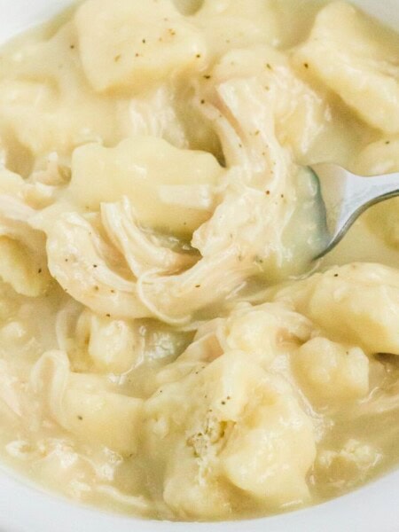 a fork lifts out a bite of Crock Pot chicken and dumplings from a white bowl.