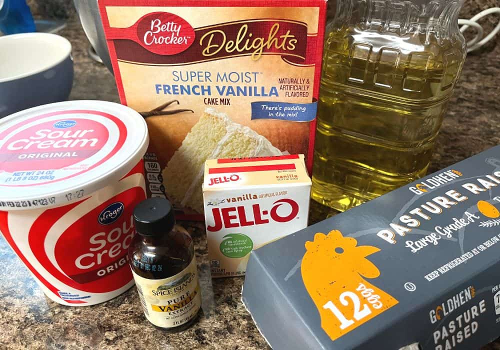ingredients for making vanilla pudding cake, including french vanilla cake mix, instant vanilla pudding mix, sour cream, oil, eggs, and vanilla extract