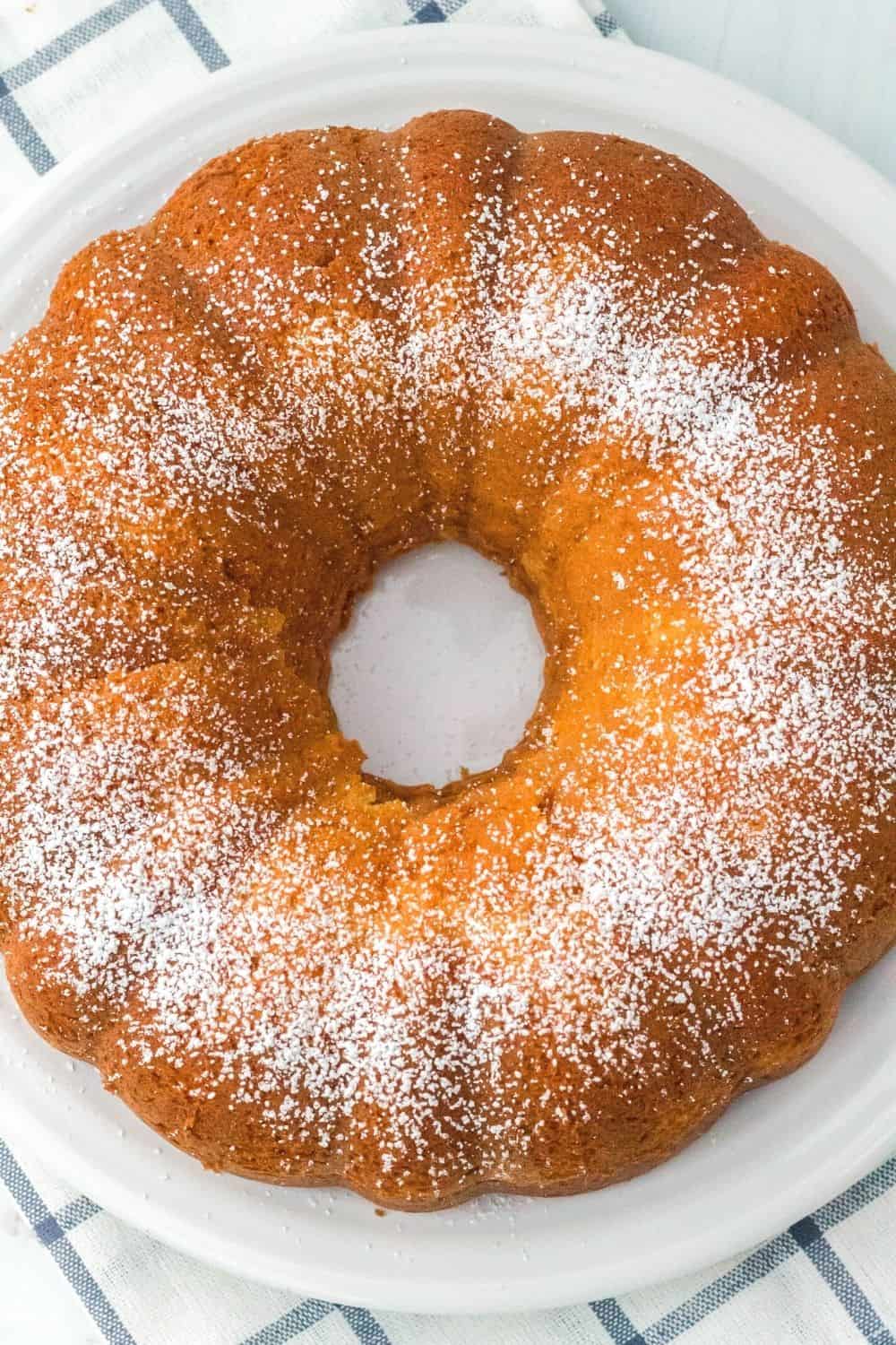 overhead view of vanilla pudding cake on a white plate, dusted with powdered sugar and ready to serve