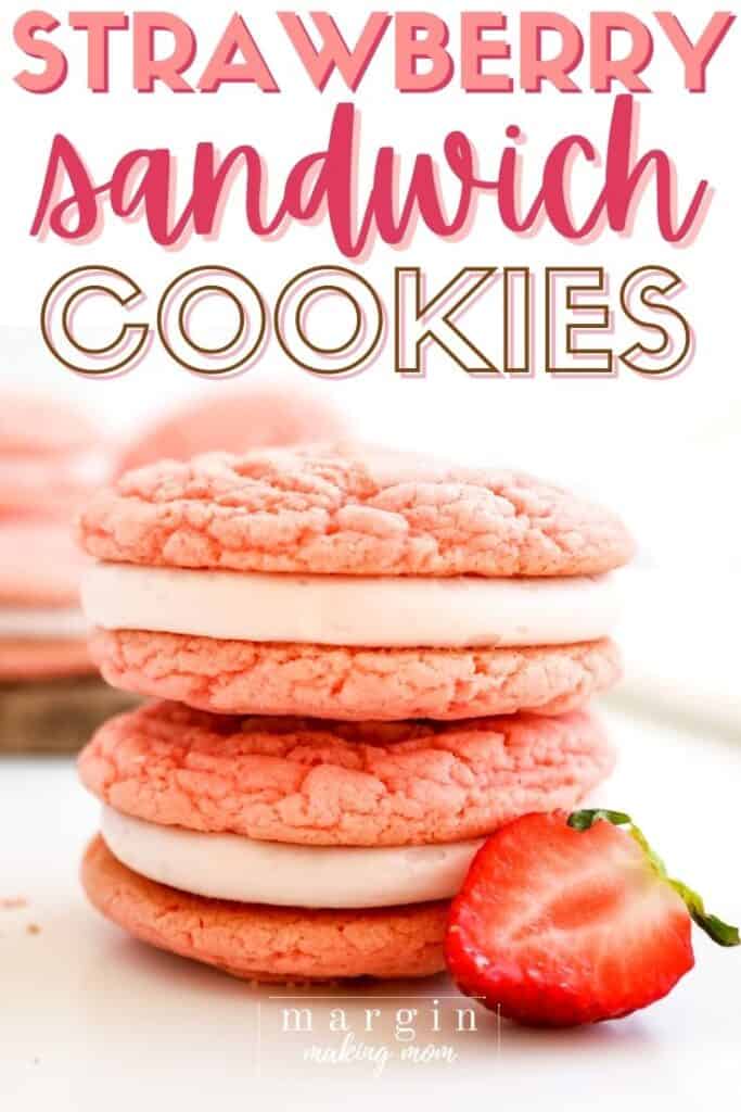 two strawberry sandwich cookies stacked on top of each other, with a halved strawberry in front.