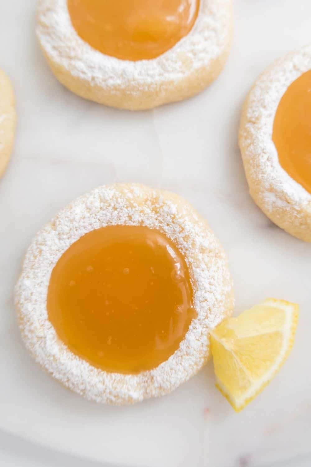 overhead view of a few lemon cookies that have been dusted with powdered sugar, showing the lemon curd filling in the center of each cookie.