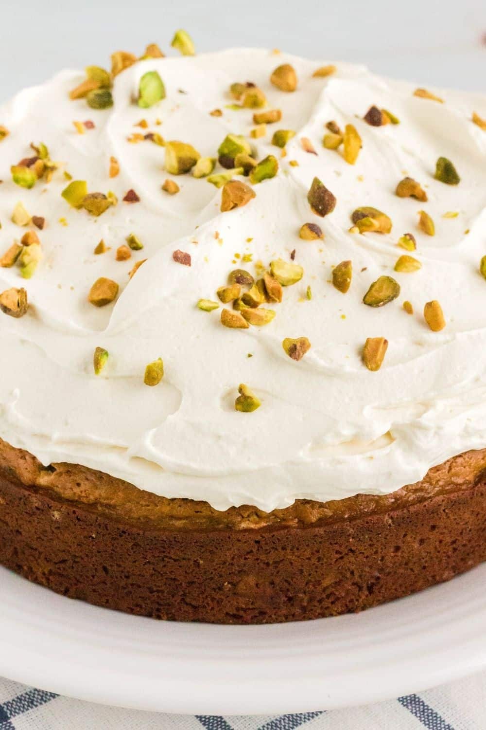 close-up view of mascarpone frosting spread on the top of a homemade pistachio cake, topped with chopped pistachio nuts.