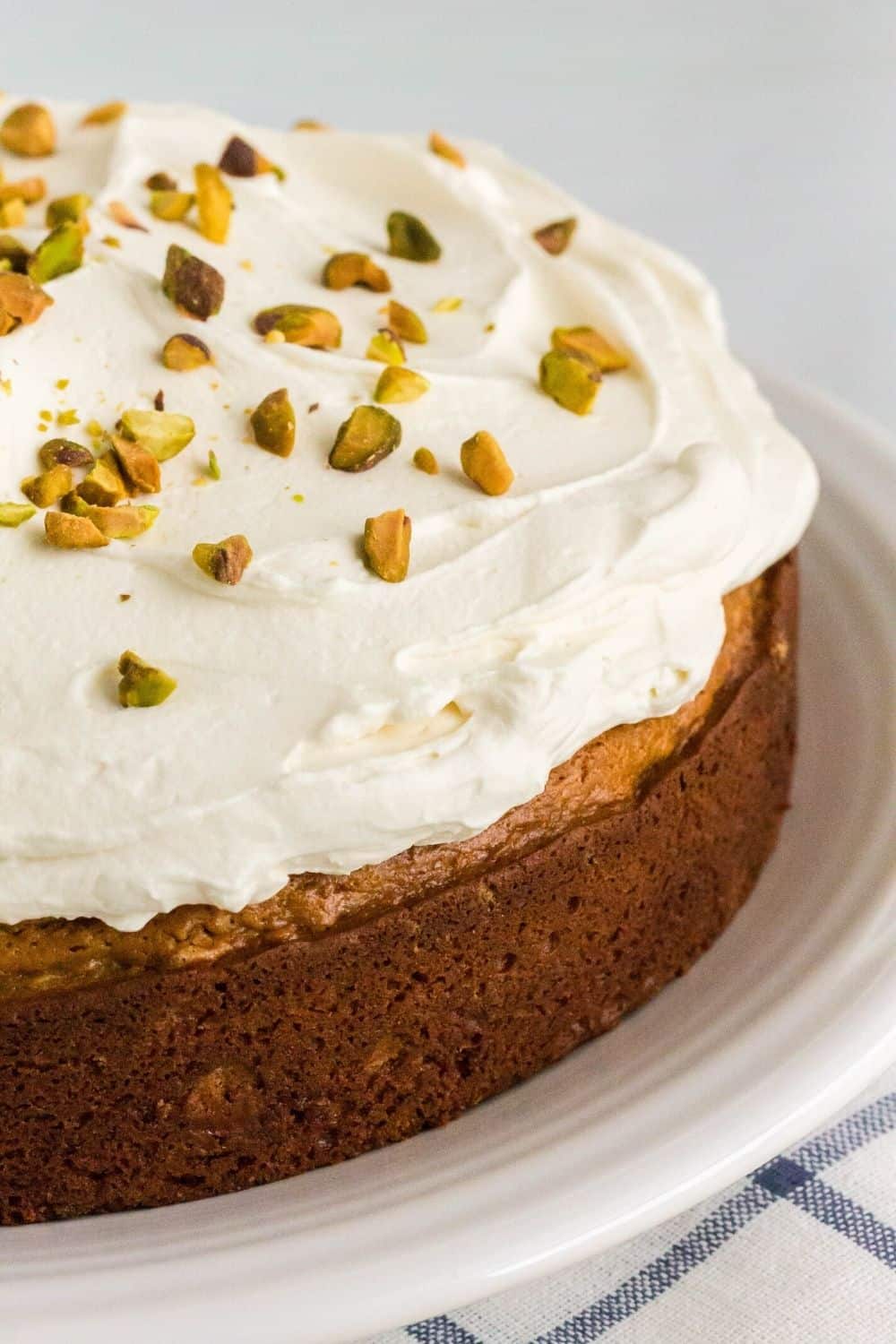 close-up view of the side of a pistachio cake layer topped with whipped mascarpone frosting and sprinkled with chopped pistachios