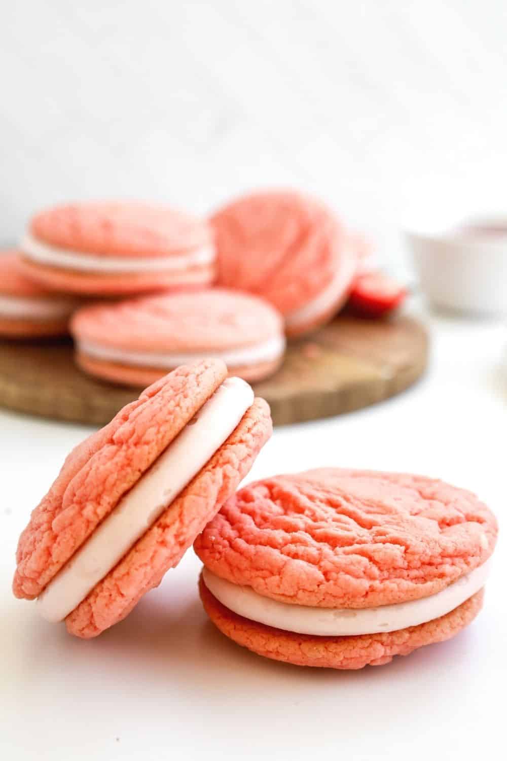 a few stacked strawberry whoopie pies in front of several other sandwich cookies in the background