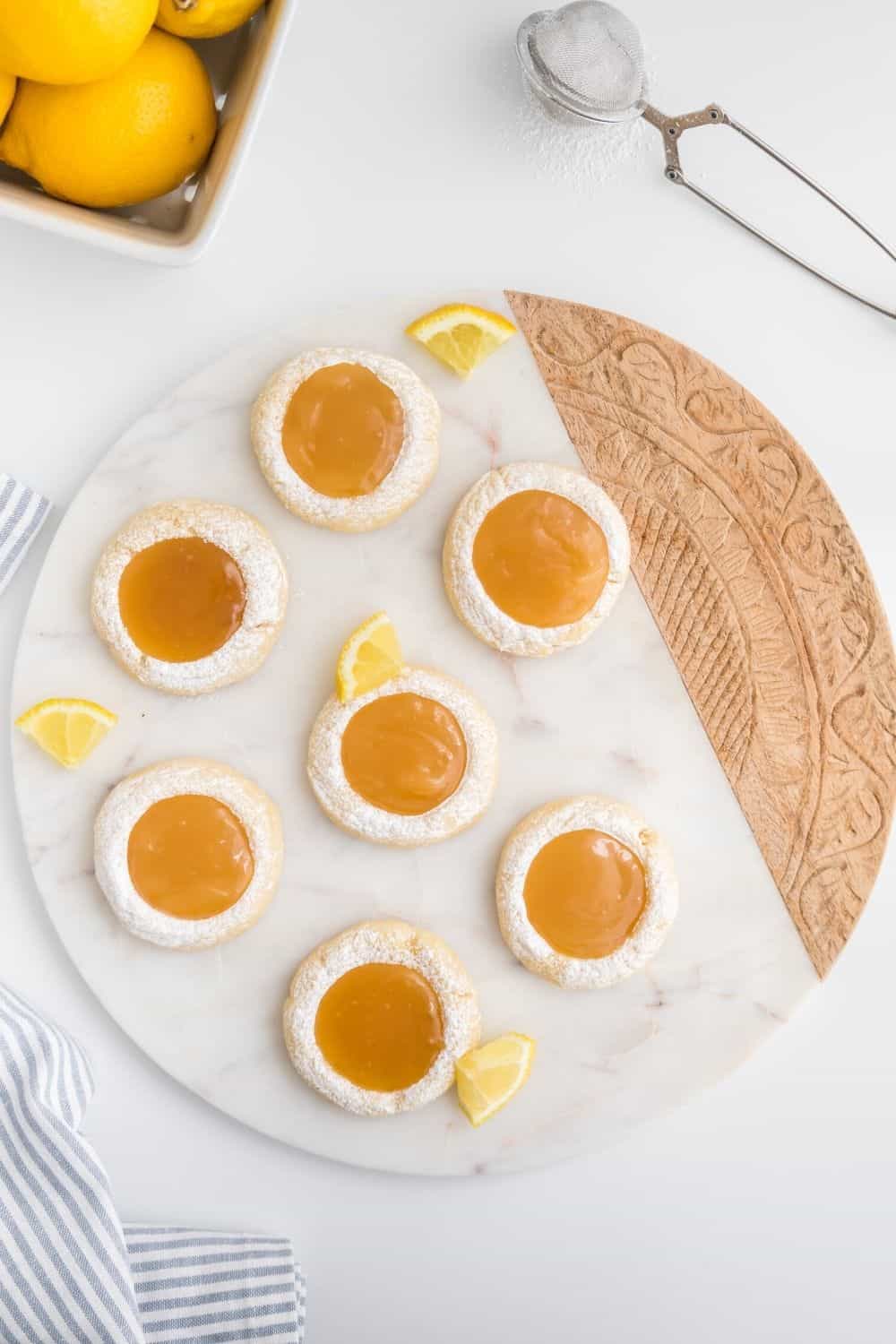 overhead view of seven lemon curd thumbprint cookies displayed on a marble serving board.