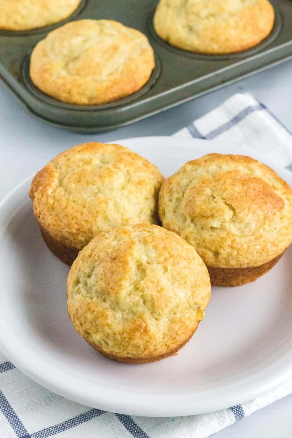 white plate with three banana muffins made with bisquick served on it. The muffin tin with remaining muffins is in the background.