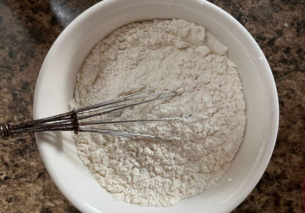 small white bowl with flour, baking soda, baking powder, salt, cinnamon, and nutmeg whisked together.