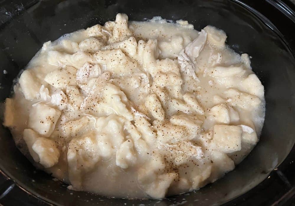 overhead view of a crock pot filled with homemade chicken and dumplings, sprinkled with black pepper