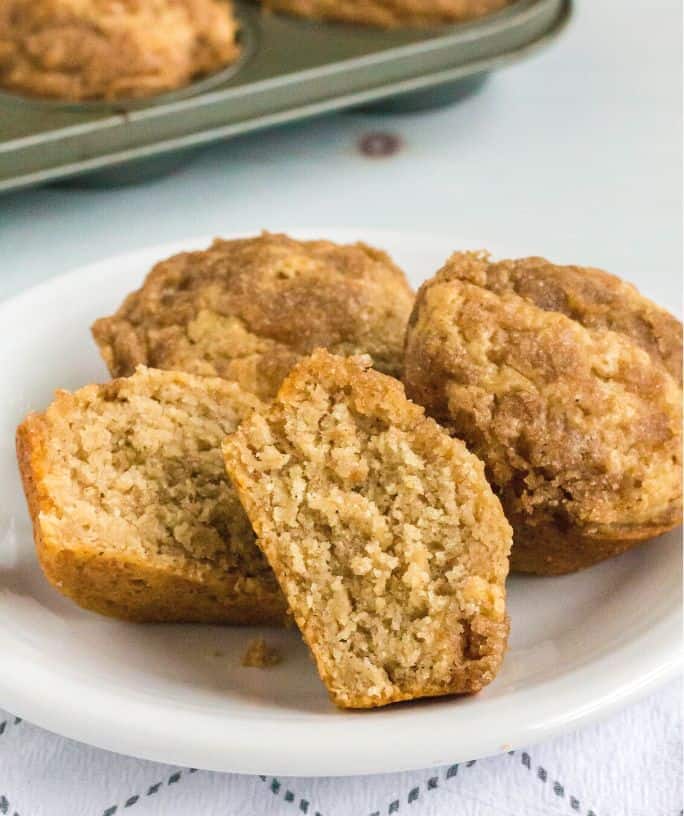 Bisquick applesauce muffins served on a white plate, with the pan of remaining muffins in the background.
