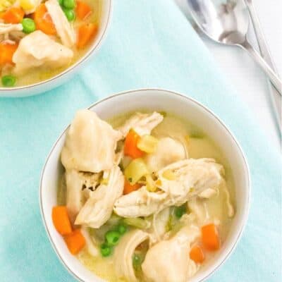 two bowls of chicken and dumplings with biscuits, with two forks nearby.