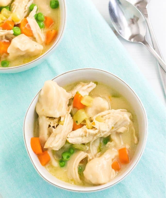 two bowls of chicken and dumplings with biscuits, with two forks nearby.