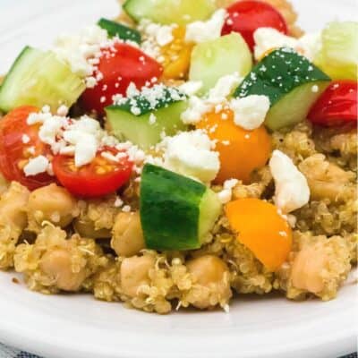 Instant Pot Greek chickpeas and quinoa served on a white plate with fresh tomatoes, cucumbers, and feta cheese