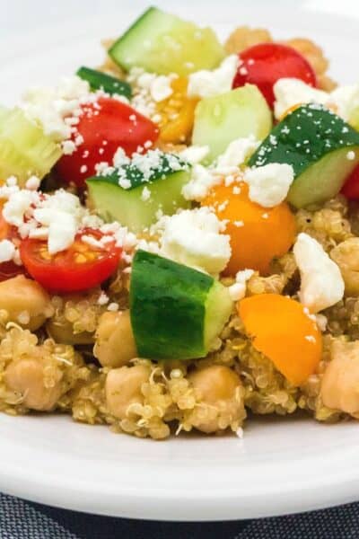 Instant Pot Greek chickpeas and quinoa served on a white plate with fresh tomatoes, cucumbers, and feta cheese