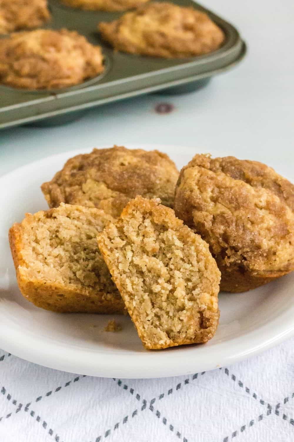 three Bisquick applesauce muffins on a white plate, one of which is cut in half to display the moist interior.