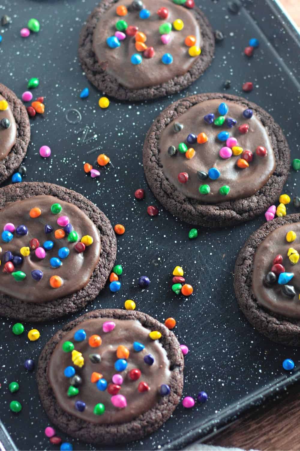 cosmic brownie fudge cookies on a baking sheet, surrounded by sprinkles