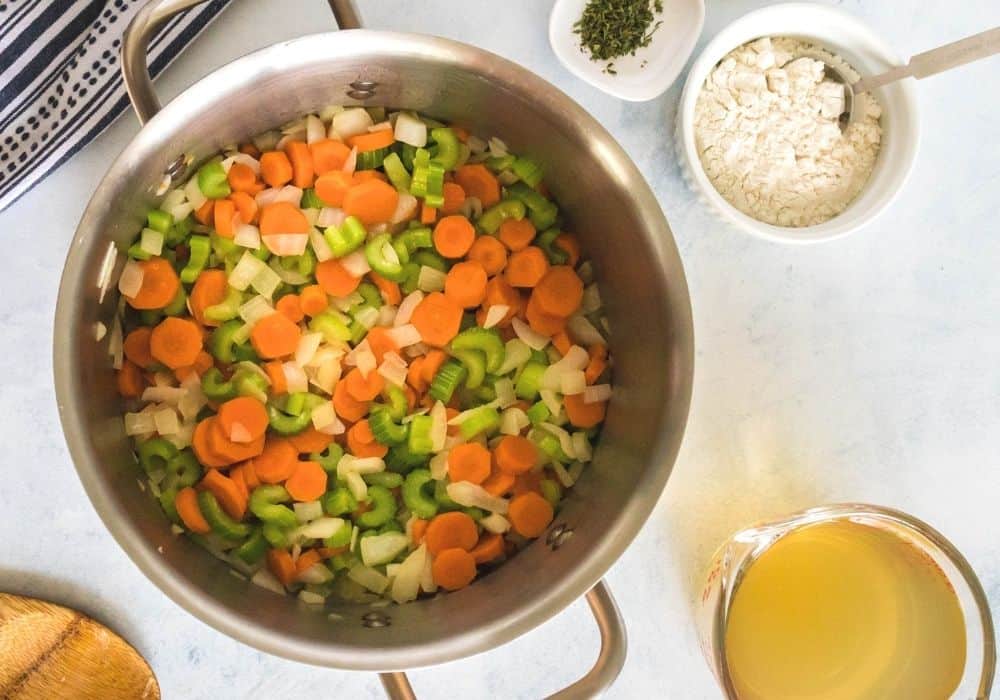 stockpot with onions, celery, and carrots being sauteed in melted butter