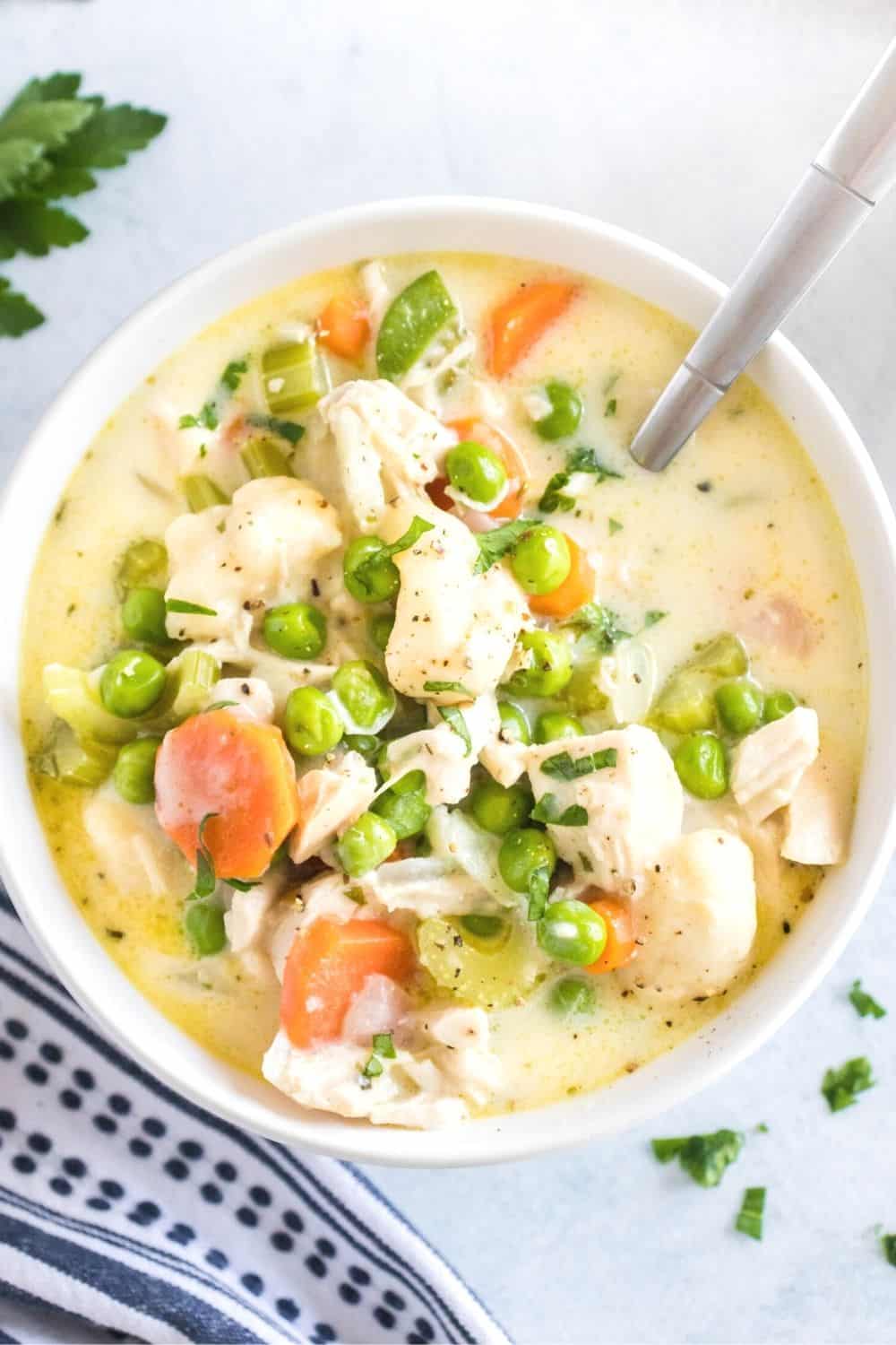 overhead view of a white bowl of chicken soup with dumplings and veggies, with a spoon in the bowl