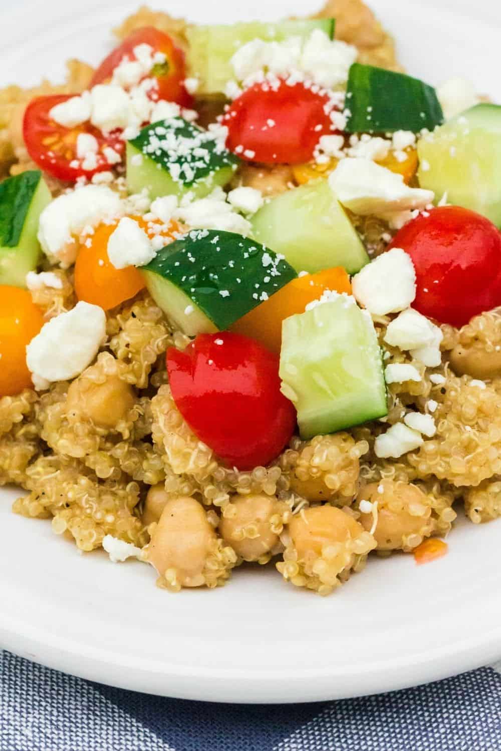 Greek chickpeas and quinoa served on a white plate, topped with cucumbers, tomatoes, and feta cheese