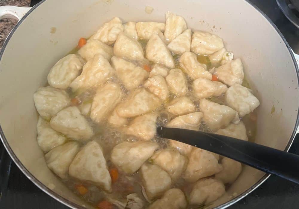 biscuit dough pieces cooking in broth in the dutch oven
