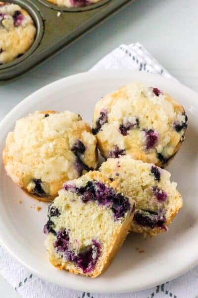 blueberry bisquick muffins on a white plate, with one muffin cut in half to show the interior.