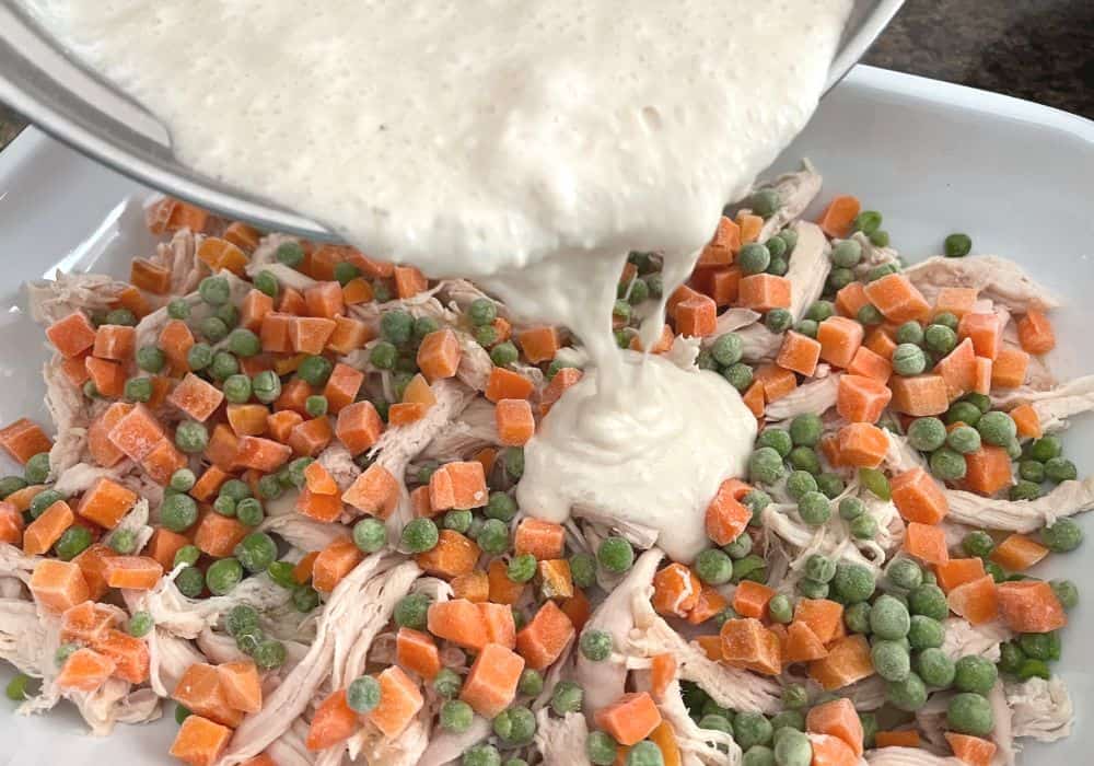 biscuit batter being poured over the chicken and veggies in a baking dish.