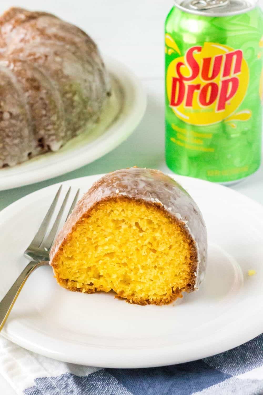 side view of a slice of SunDrop bundt cake served on a white plate with a fork. A can of SunDrop is in the background.