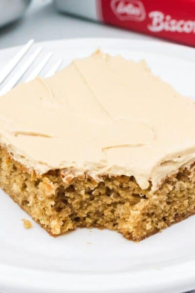 a slice of Biscoff cake served on a white plate. A bite has been taken out of the cake, which is topped with cookie butter frosting.