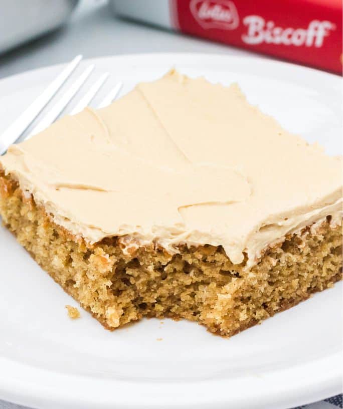 a slice of Biscoff cake served on a white plate. A bite has been taken out of the cake, which is topped with cookie butter frosting.