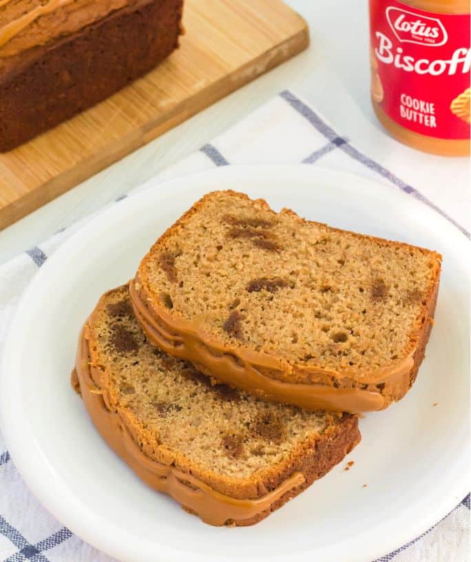 two slices of biscoff loaf cake on a white plate, with a jar of Biscoff spread in the background and the remaining cake on a cutting board.