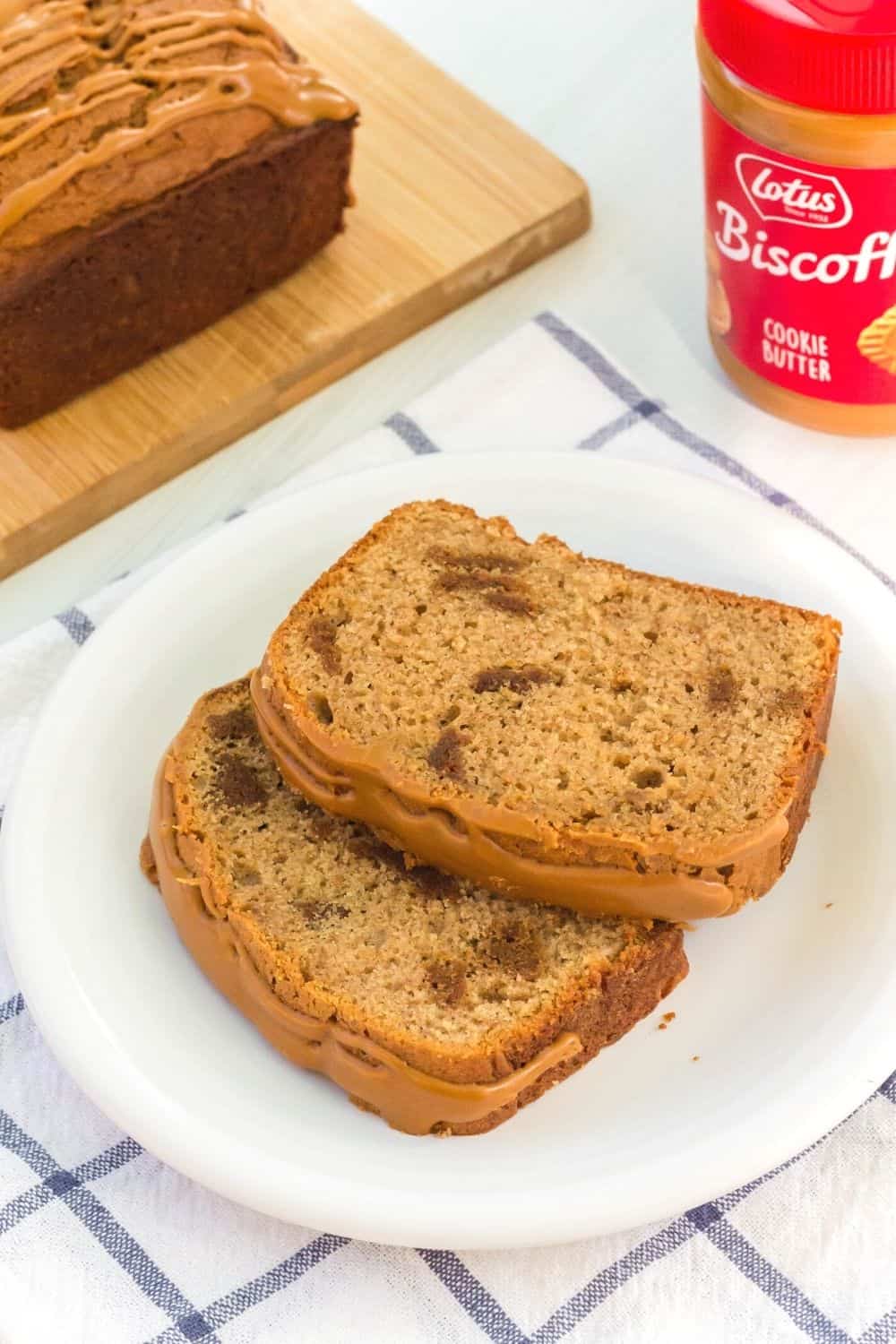 two slices of Biscoff loaf cake served on a white plate, with the remaining cake and a jar of Biscoff spread in the background.