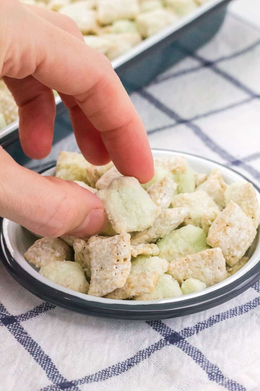a woman's hand reaches into a small round dish of pistachio muddy buddies snack mix