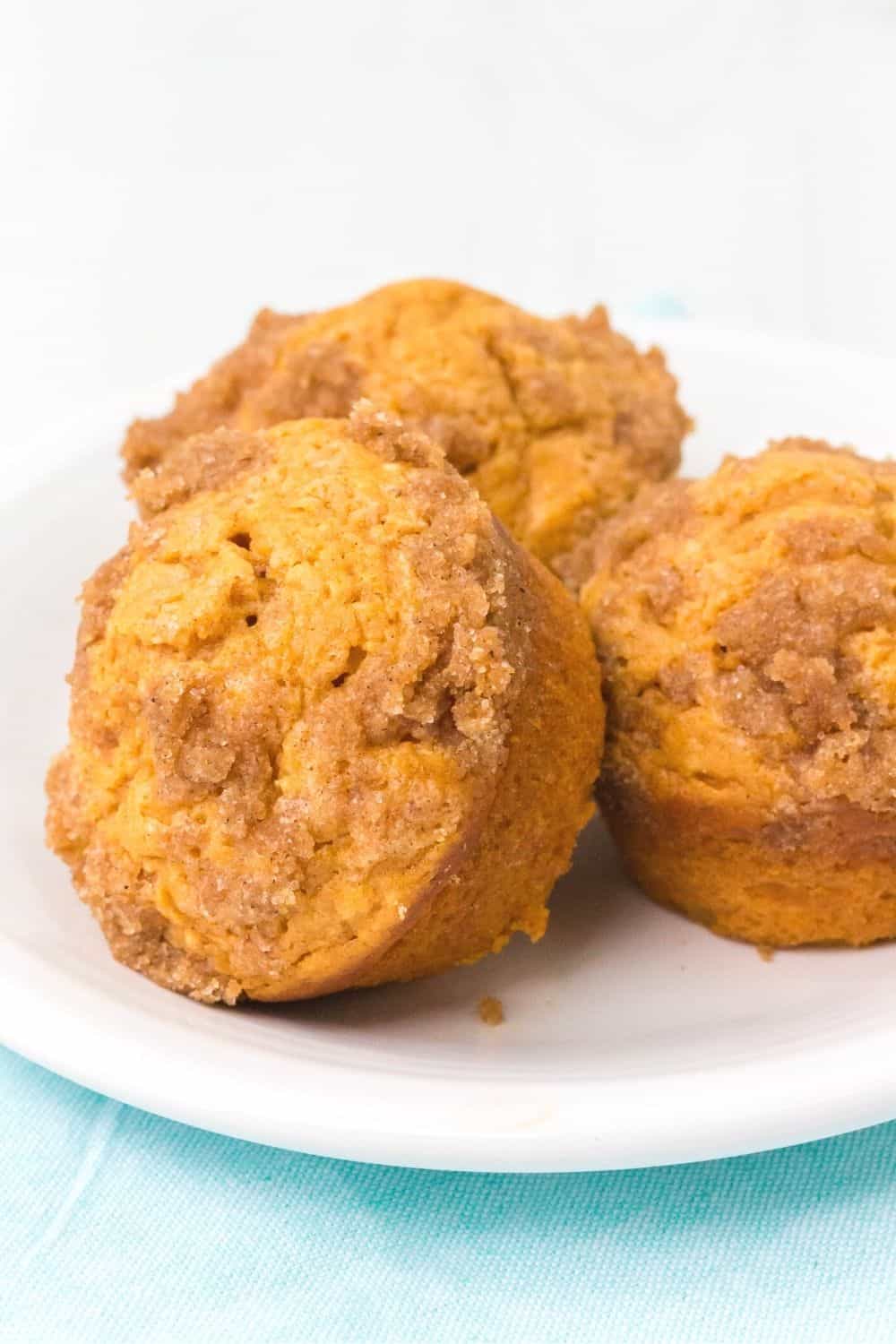 three homemade sweet potato muffins topped with cinnamon sugar streusel, served on a white plate.